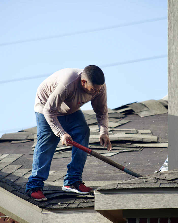 Worker removing damaged shingles from a house roof